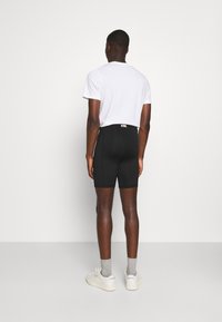 Sorte stretchshorts, glat tekstur, tætsiddende design, parret med en ensfarvet hvid t-shirt, hvide sneakers og grå sokker.