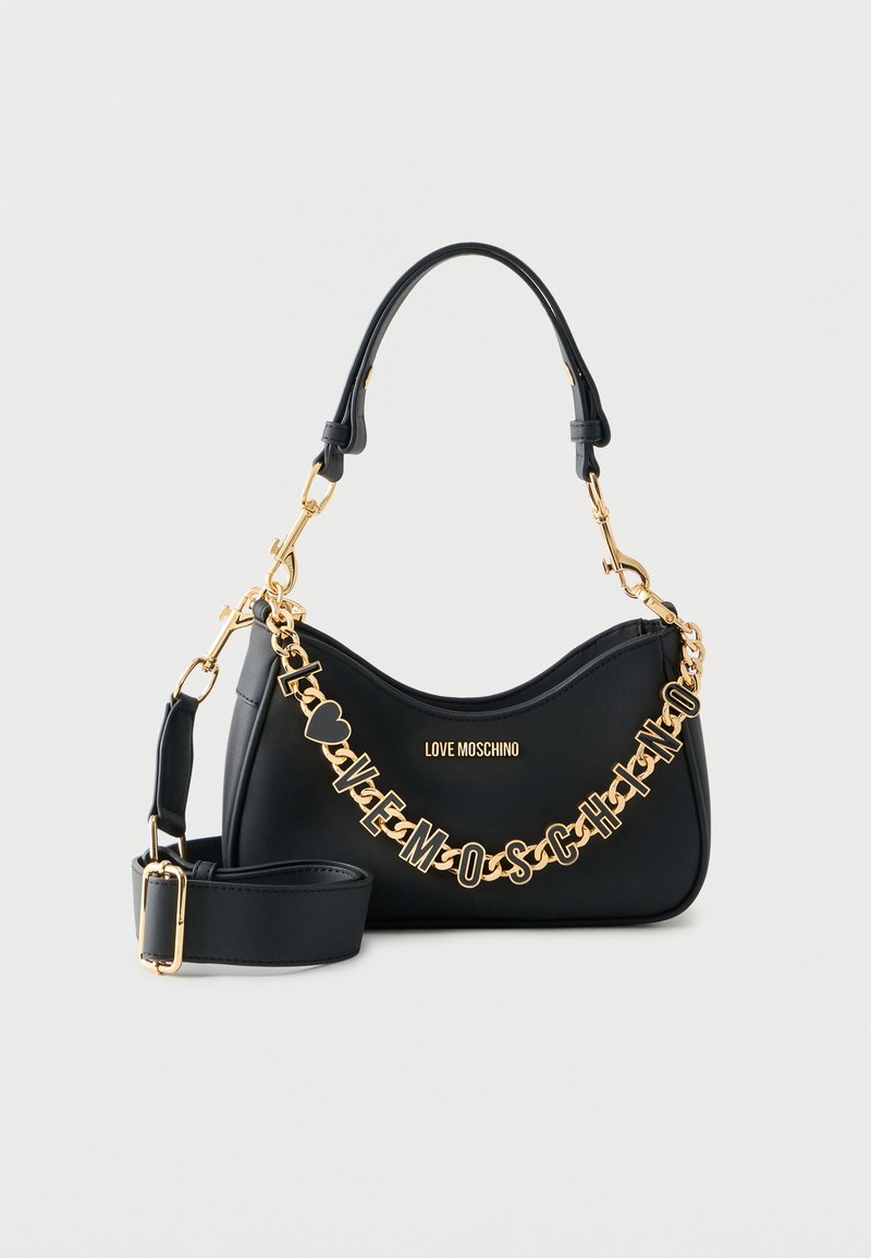 Μαύρη τσάντα Moschino με χρυσή αλυσίδα που σχηματίζει το όνομα της μάρκας, αποσπώμενος ιμάντας ώμου και κυρτή κορυφαία λαβή σε λευκό φόντο.