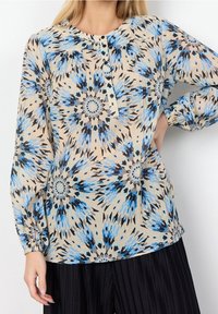 Blusa leggera e con motivo floreale in blu e nero su sfondo beige, con maniche lunghe e scollatura con bottoni.