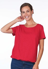 Red short-sleeve t-shirt with a round neckline, lightweight, slightly slubbed texture, and relaxed fit, paired with dark blue jeans.