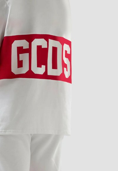 Valkea vaatetus, jossa on rohkea punainen vaakasuora raita ja suuret valkoiset lohkokirjaimet "GCDS" selkäpuolella.