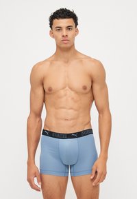 Kék boxernadrág fekete elasztikus derékpánttal, rajta a "PUMA" logo. Simaság jellemzi, testhezálló fazonnal és combközép hosszúsággal, varrás nélkül.