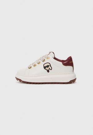 Biały sneaker z bordo podeszwą i wyściółką, złotymi oczkami, wzorzystymi sznurówkami oraz małym kreskówkowym logo osoby noszącej okulary przeciwsłoneczne z boku.