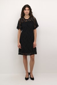 Black lace dress with short flutter sleeves, knee-length, scalloped hem, and floral pattern. Worn with black high-heeled shoes.