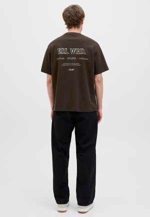 Brown cotton t-shirt with white text on back; relaxed fit. Paired with black wide-leg pants and white sneakers. Simple design, no patterns.