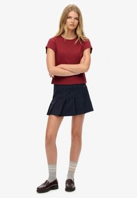 Rød kortærmet t-shirt, marineblå stribede plisserede nederdel, grå stribede sokker og bordeaux loafers. Afslappet outfit med rene linjer og kontrasterende farver.