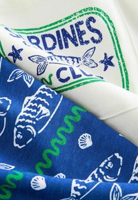 Two fabric pieces stacked: one white with green and blue fish graphics, the other blue with white fish and shell patterns. Textured cotton blend.