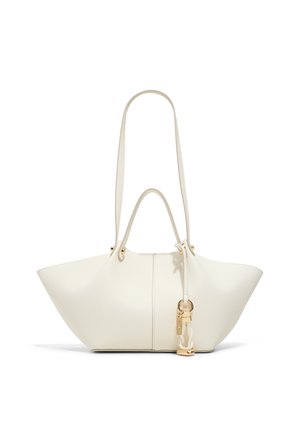 Sac cabas en cuir blanc avec une large forme trapézoïdale, double anses, longue bandoulière et un pendentif doré suspendu sur le côté.
