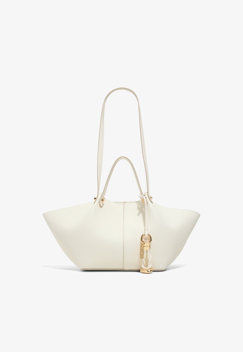 Sac cabas en cuir blanc avec une large forme trapézoïdale, double anses, longue bandoulière et un pendentif doré suspendu sur le côté.