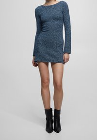 Abito lungo a maniche lunghe blu a coste con scollo rotondo, silhouette aderente e orlo sopra la coscia. Indossato con stivali neri alla caviglia.