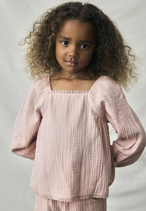Top in cotone texturizzato rosa con scollatura quadrata, lunghe maniche a sbuffo e pizzo lungo l'orlo. Modella con capelli ricci in piedi.