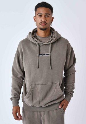 Hoodie grigio oversize realizzato in tessuto morbido, con tasca frontale, cappuccio con coulisse e un piccolo logo al centro. Polsini e orlo a coste.