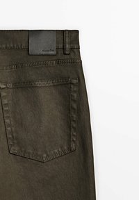 Olijfgroene denim broek met een rechthoekig zwart leren label op de taille en een genaaide zak op de achterkant, met zichtbare stikseldetails.