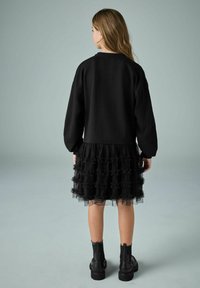 Must have oversize mustar, millekerge mustast tüllist kleit, millel on volangid, kantud koos mustade pahklépatside kingadega. Sile kangas ja tekstureeritud kihid.