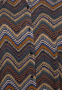 Camicia con motivo a onde nei colori blu, arancione e crema. Realizzata in tessuto testurizzato con righe verticali e bottoni neri.