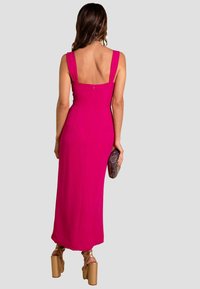 Vestido maxi fucsia con tirantes anchos, corpete ajustado y cierre con cremallera en la parte posterior. Combinado con un bolso texturizado y tacones de plataforma alta.