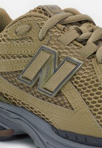 Gros plan d'une chaussure de sport marron et grise avec un tissu en maille, des lacets épais et un grand logo « N » sur le côté.