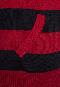 Maglione a righe rosse e nere con una piccola tasca, texture a coste e design aderente.
