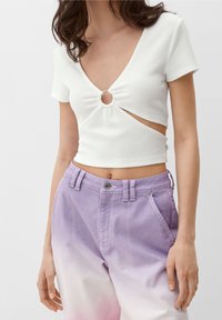 Bílý žebrovaný crop top s hlubokým véčkovým výstřihem a předním výřezem, zdobený stříbrným kroužkem. V páru s kalhotami v levandulovém ombre a předními kapsami.