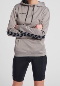 Grå huvtröja med ribbad textur och huva, med svarta chevronmönster längs ärmarna, tillsammans med svarta åtsittande shorts.