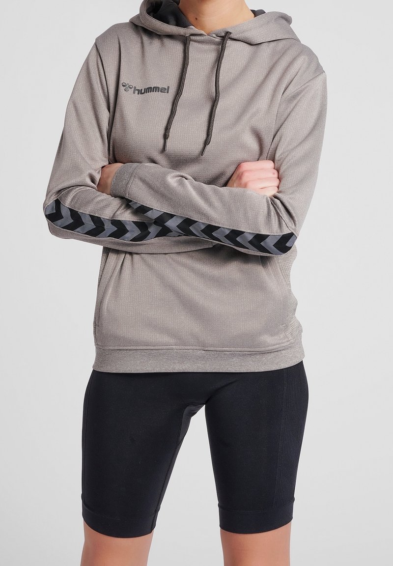 Grå huvtröja med ribbad textur och huva, med svarta chevronmönster längs ärmarna, tillsammans med svarta åtsittande shorts.