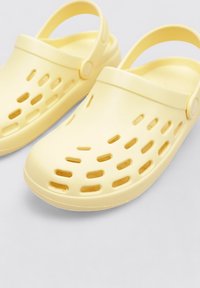 Sabots en caoutchouc jaunes avec des trous de ventilation et une sangle à l'arrière. Bout arrondi et texture lisse. Design flexible et léger pour le confort.
