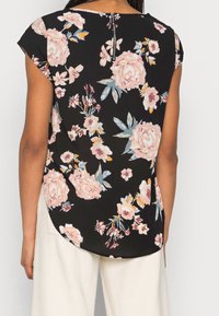 Blusa nera a fiori con motivi di fiori rosa e blu, maniche corte e chiusura con zip sul retro. L'orlo curvo aggiunge un tocco di dettaglio.