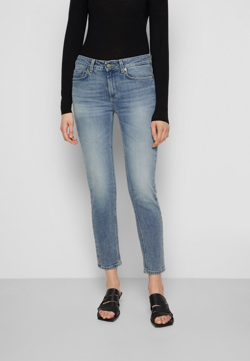 Jeans de color azul claro con un corte ajustado, detalles de desvanecimiento, diseño de cinco bolsillos y cierre de botón, combinados con sandalias negras de tiras.