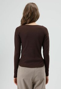 Donkerbruine geribbelde top met lange mouwen en ronde hals, getailleerde pasvorm en gladde textuur, gecombineerd met beige broek.