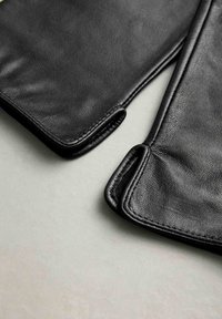 Sorte læderhandsker med en glat tekstur, der har afrundede kanter og kontrasterende syninger. Nærbillede, der fremhæver materialet og designdetaljerne.