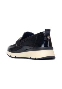 Zapato negro de charol sin cordones con un patrón texturizado, punta redondeada y suela de goma blanca. Presenta un pequeño logo redondo en el talón.