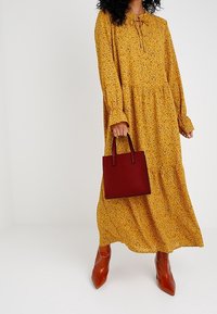 Pitkähiha, sinapinkeltainen mekko, jossa on kukkakuosi, frillireunaiset hihansuut ja kerroksellinen hame. Yhdistetty pieneen punaiseen käsilaukkuun ja ruskeisiin korkokenkiin.