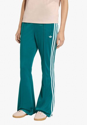 Pantaloni della tuta color teal con design a tre strisce bianche, realizzati in tessuto liscio. Presentano una gamba svasata e un logo ricamato sulla parte anteriore.