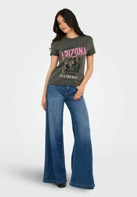Camiseta gráfica de color verde oscuro con texto rosa e ilustración de un caballo; combinada con jeans de pierna ancha de lavado medio, con tejido texturizado.