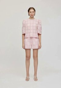 Conjunto de duas peças com um top rosa de renda com mangas balão e calções a condizer. O tecido é leve e texturizado com padrões de grelha.