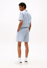 Lys blå kortermet skjorte og matchende shorts med et subtilt mønster. Skjorten har krage og lommer, kombinert med hvite joggesko.