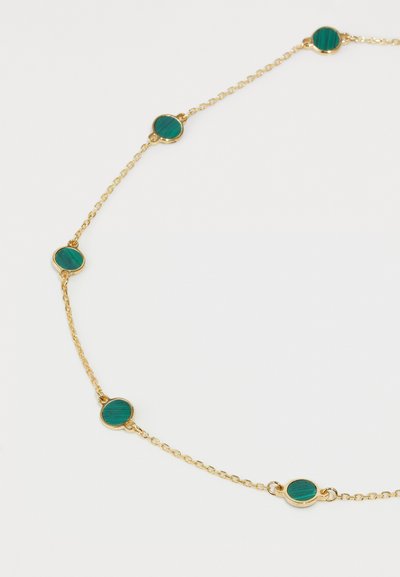 Zelta ķēdīte ar apaļām malahīta akmeņiem, kas vienmērīgi izkārtoti. Gluda tekstūra ar pulētu apdari un minimālistisks dizains.