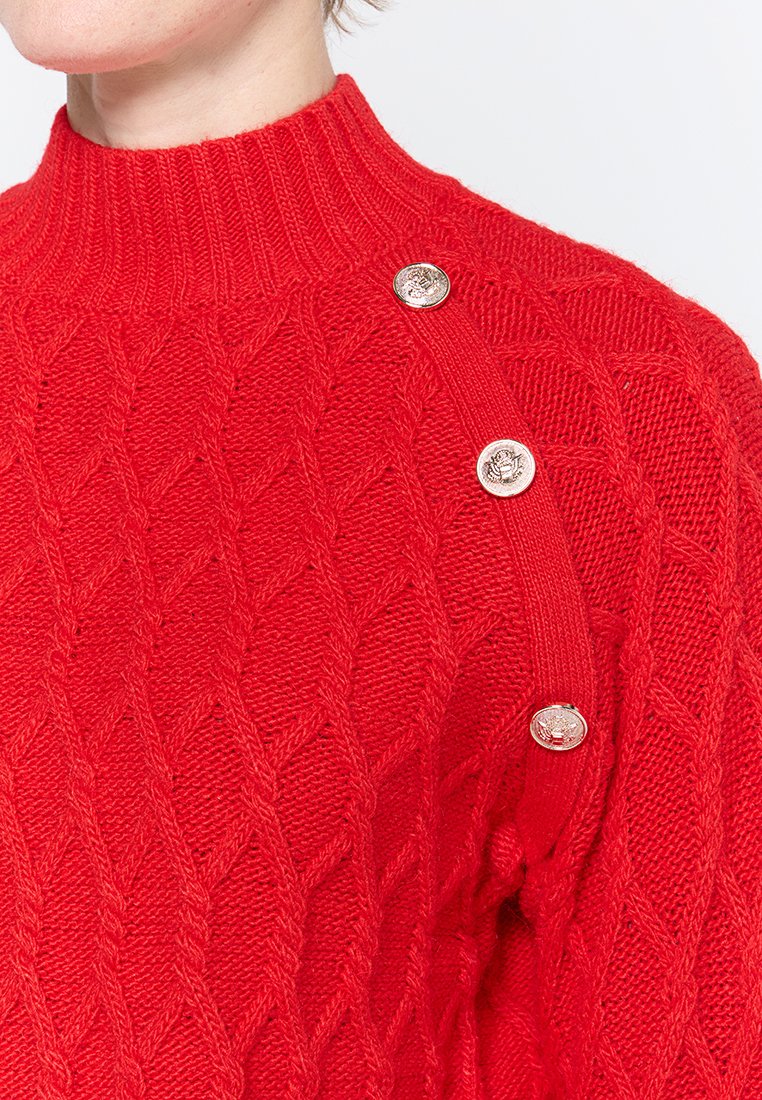 Maglione rosso lavorato a maglia con collo alto, motivo a diamante testurizzato e tre bottoni metallici sulla spalla sinistra.