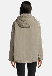 Hellbeige Kapuzenjacke mit lockerer Passform, die über eine glatte Textur, Druckknopfverschlüsse und ein gesticktes Logo auf der Rückseite verfügt.