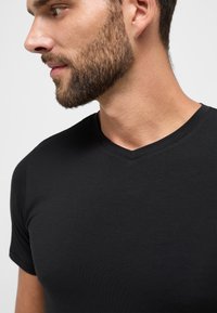Sort V-hals t-shirt, korte ærmer, tætsiddende design, blød tekstur, glat stof, ingen synlige mønstre eller logoer. Nærbillede af halsudskæring.