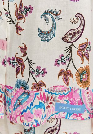 Biely textil s multikolórovými kvetinovými vzormi v odtieňoch ružovej, modrej a hnedej. Obsahuje lemovú nálepku s nápisom "BOHO PRERIE" v modrej farbe.