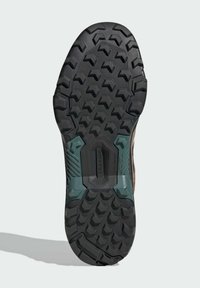 Black rubber outsole with deep traction grooves, textured surface, reinforced heel, and teal accents. Designed for grip and durability.