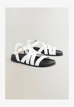 Weiße Sandalen mit Riemen und schwarzen Sohlen, ausgestattet mit breiten Riemen, einer verstellbaren Schnalle und einem flachen Design, das sich für das tägliche Tragen eignet.