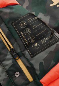 Camouflage jacket featuring a water-resistant label, a gold zipper, and a textured orange accent. Includes waterproof and windproof details.