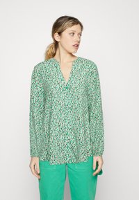 Groene gebloemde blouse met een V-hals en lange mouwen, met een losse pasvorm en kleine knopen, gecombineerd met turquoise broek.