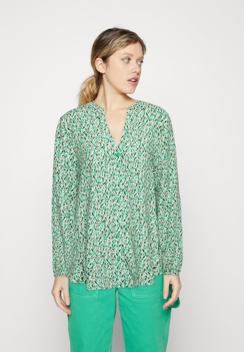Groene gebloemde blouse met een V-hals en lange mouwen, met een losse pasvorm en kleine knopen, gecombineerd met turquoise broek.