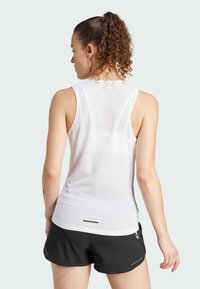 Witte sportieve tanktop van mesh met een ronde hals en racerback ontwerp, gecombineerd met zwarte shorts met reflecterende accenten.