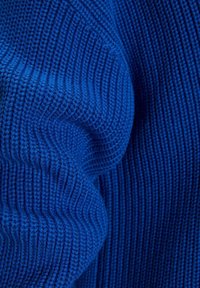 Tissu tricoté bleu avec une texture côtelée, montrant des plis et des motifs de points détaillés.