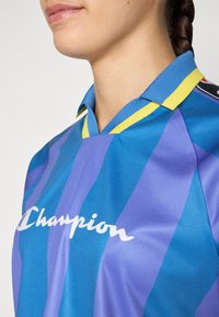 Könnyű kék mez, vertikális csíkokkal eltérő árnyalatokban, sárga gallérral és fehér "Champion" logóval az elején.