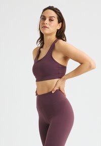 Lila Sport-BH und hoch-taillierte Leggings aus dehnbarem Material. Das Design verfügt über breite Träger und eine glatte Textur ohne Muster.